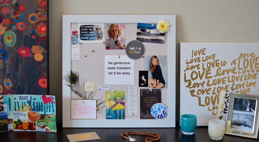 Framed physical vision board with printed photos, quotes, postcards, and handwritten notes on a shelf